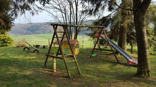 Speelveld voor de deur met schommels, glijbaan, zandbak, speelhuisje,en een wip.